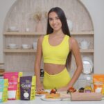 Young woman in a yellow activewear set standing in a modern kitchen, displaying a range of Livsmart natural sweeteners including Monk Fruit, Erythritol, Allulose, and Stevia